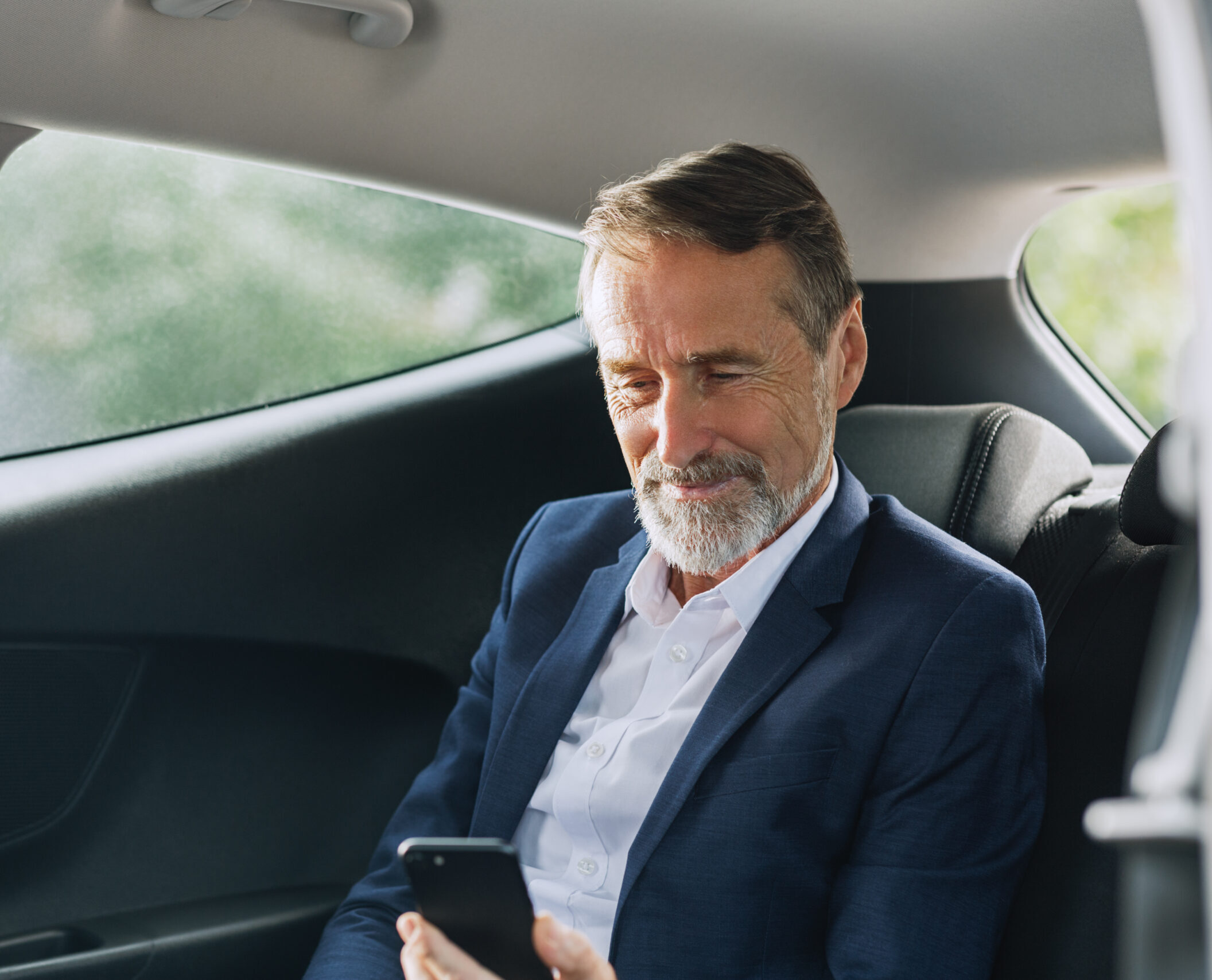 Businessman sitting in the car using a smartphone. Man checking cell phone on a backseat.